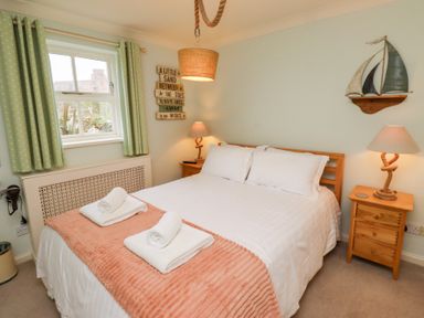 A bedroom with a double bed nightstands with lamps window with green curtains and wall decorations at The Wynd in Bamburgh