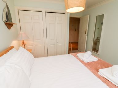A bedroom with a double bed with white linens and towels on a peach blanket bedside table with lamp closets with white doors a wall mirror and a model sailboat on a shelf at The Wynd in Bamburgh