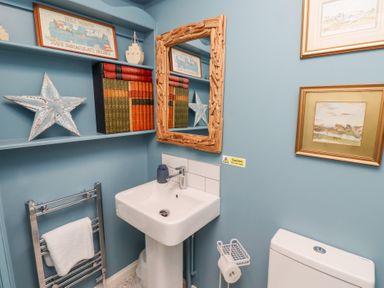 A bathroom with blue walls a white sink a wooden framed mirror shelves with books and decorations at The Wynd in Bamburgh