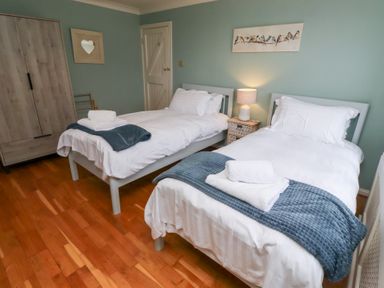 A bedroom with two single beds with white linens and blue blankets a bedside table with a lamp a wardrobe and a bird painting on the wall at The Wynd in Bamburgh