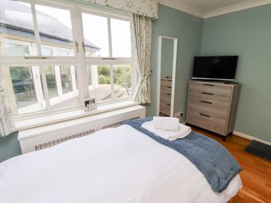 A bedroom with a bed covered by white and blue bedding a chest of drawers with a television and a window with curtains at The Wynd in Bamburgh