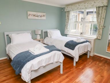 A bedroom with two single beds a nightstand with a lamp a window with curtains and a wall painting at The Wynd in Bamburgh