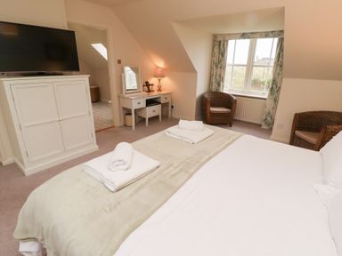 A bedroom with a bed towels on it a white cabinet with a television a desk with a lamp two wicker chairs and a window at The Wynd in Bamburgh