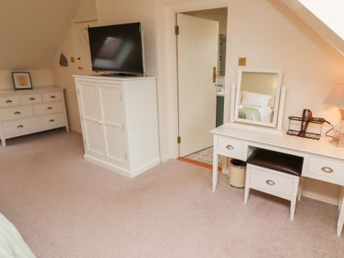 A bedroom area with a white TV cabinet and a television a dresser with drawers and a framed picture a vanity table with a mirror hairdryer and a lamp at The Wynd in Bamburgh