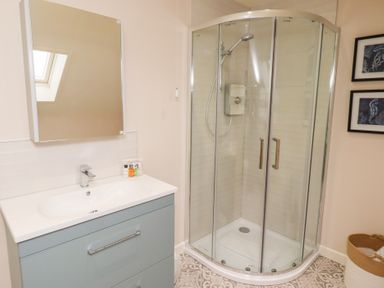 A bathroom with a sink and mirror cabinet next to a glass shower enclosure at The Wynd in Bamburgh