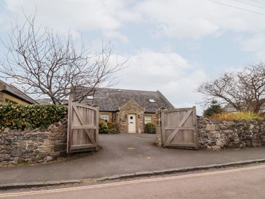 A stone house with an open wooden gate and stone walls on either side at The Wynd in Bamburgh