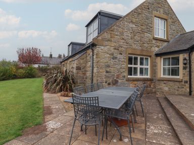 An outdoor patio with a metal table and chairs beside a stone house and garden at The Wynd in Bamburgh