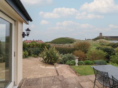 A garden with patio furniture plants and a birdbath with hills and houses in the background at The Wynd in Bamburgh