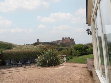 An outdoor garden area with black chairs and a large plant overlooking a historic castle at The Wynd in Bamburgh