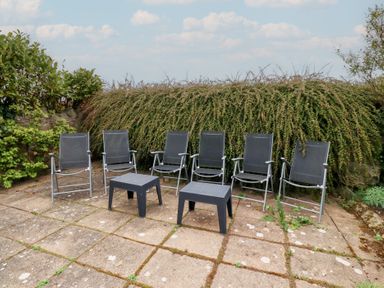 An outdoor patio area with six black chairs and two small tables in front of a hedge at The Wynd in Bamburgh