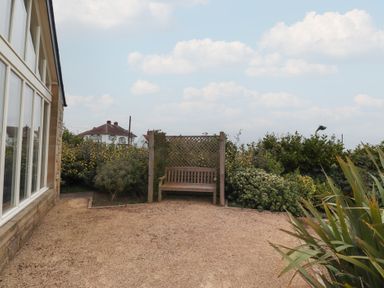 An outdoor area with a wooden bench against a lattice screen and surrounded by bushes at The Wynd in Bamburgh