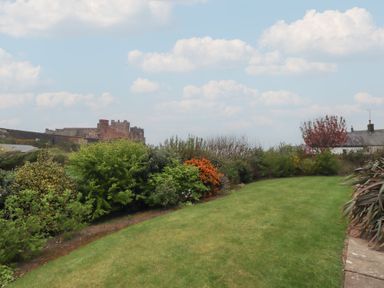 A garden with shrubs and grass with a castle in the background at The Wynd in Bamburgh