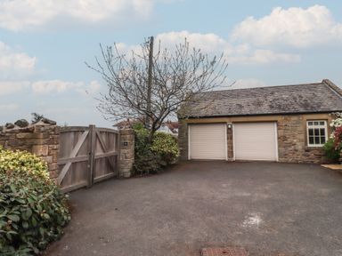 A driveway with closed wooden gates and a double garage with roller doors at The Wynd in Bamburgh