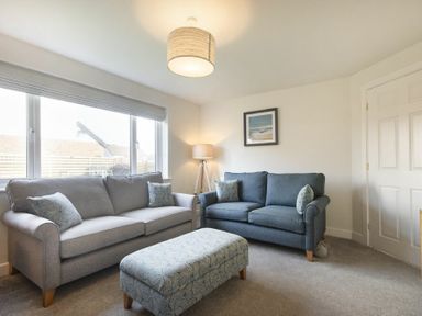 A living room with two sofas a patterned ottoman a floor lamp and a framed picture at Luna Tide in Seahouses