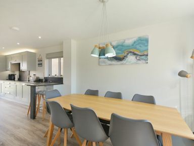 A dining area with a wooden table and gray chairs next to a kitchen with gray cabinets and a black countertop at Luna Tide in Seahouses
