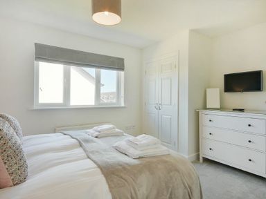A bedroom with a bed folded towels a dresser and a wall mounted television at Luna Tide in Seahouses