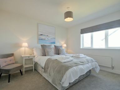 A bedroom with a bed towels on it beside two bedside tables with lamps and a chair by the wall at Luna Tide in Seahouses