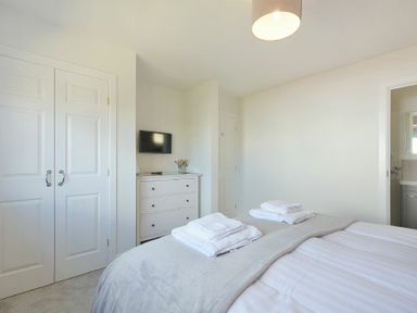 A bedroom with a bed and towels on it a dresser with a TV and flowers on top and doors at Luna Tide in Seahouses