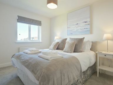 A bedroom with a double bed pillows bedside tables lamps and a window at Luna Tide in Seahouses