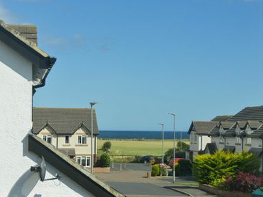 A residential street with houses cars and a grassy field with the sea in the background at Luna Tide in Seahouses