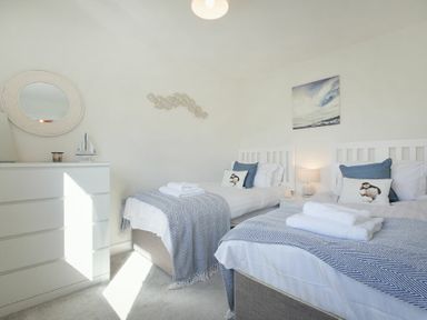 A bedroom with two single beds each with towels pillows and a bedside table lamp at Luna Tide in Seahouses