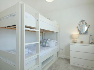 A bedroom with a white bunk bed and a white dresser with a lamp and decorative items at Luna Tide in Seahouses