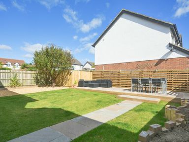 A backyard with a grass lawn a stone path a tree outdoor seating and dining area at Luna Tide in Seahouses
