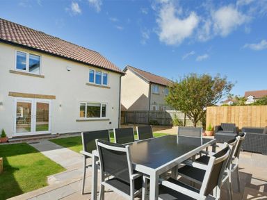 A backyard with a patio dining table and chairs a lawn and houses in the background at Luna Tide in Seahouses