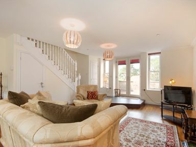 A living room with sofas, armchair, rug, TV on stand, staircase, and glass doors at The Old Concert Room in Alnmouth
