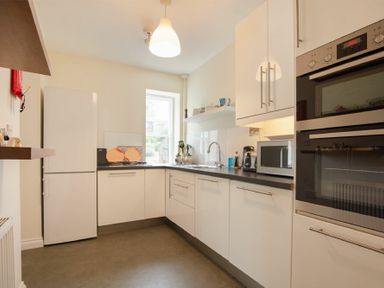 A kitchen with white cabinets appliances and a window at The Old Concert Room in Alnmouth