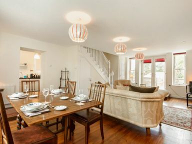 A dining area with a wooden table set for four and a living area with beige sofas near stairs at The Old Concert Room in Alnmouth