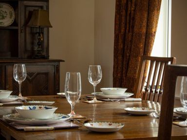 A dining room with a wooden table set with bowls plates wine glasses and cutlery at The Old Concert Room in Alnmouth