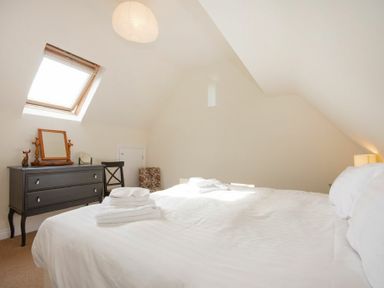 A bedroom with a double bed white linens a black dresser a chair and a skylight window at The Old Concert Room in Alnmouth