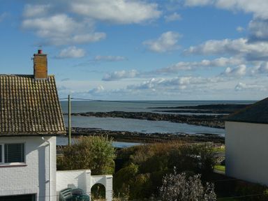 Sea view with rocky shore and clouds above with parts of white houses and garden bushes nearby at Coast View in Beadnell
