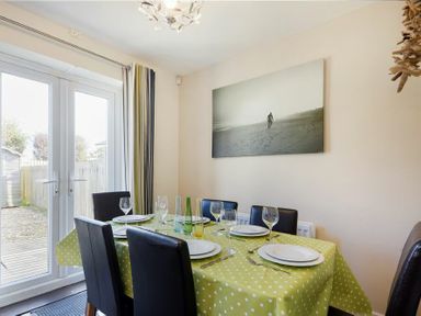 A dining room with a table set for six people and glass doors leading outside at Coast View in Beadnell
