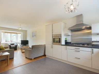 An open plan kitchen and living area with a stove oven cabinets sofa chairs and a television at Coast View in Beadnell