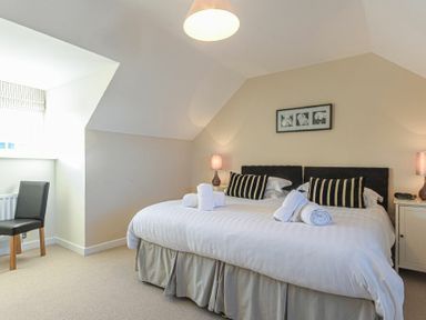 A bedroom with a double bed with striped pillows and rolled towels a chair and bedside tables at Coast View in Beadnell
