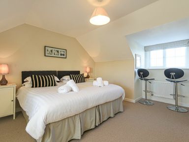 A bedroom with a double bed two bedside tables with lamps and two stools by a window at Coast View in Beadnell