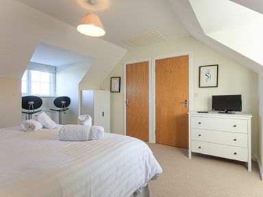 A bedroom with a bed with towels a window with two chairs two wooden doors and a chest of drawers with a TV at Coast View in Beadnell