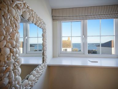 A window with a view of the sea and houses and a mirror with a shell frame in a room at Coast View in Beadnell