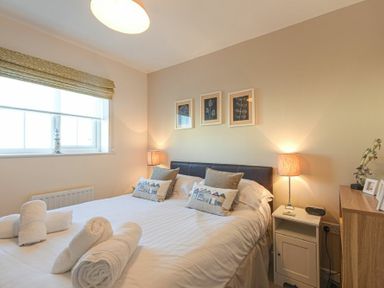 A bedroom with a bed with pillows and rolled towels beside a window with a valance at Coast View in Beadnell
