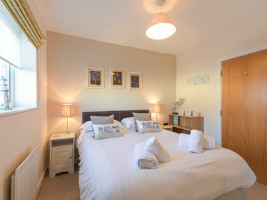 A bedroom with a double bed bedside tables lamps and framed pictures on the wall at Coast View in Beadnell