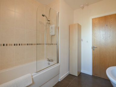 A bathroom with a bathtub and shower unit a wooden storage cabinet and a wooden door at Coast View in Beadnell