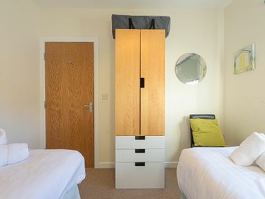 A bedroom with two single beds a wooden wardrobe a wooden door and a chair with a green cushion at Coast View in Beadnell