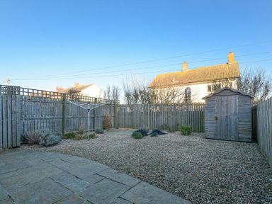 A backyard with a stone patio a clothesline a wooden shed and a gravel area surrounded by a wooden fence at Coast View in Beadnell