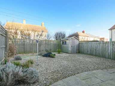 A backyard with gravel ground a wooden shed and a rotary clothesline fenced by wooden panels at Coast View in Beadnell