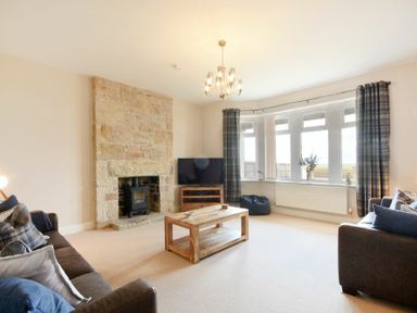 A living room with a stone fireplace a wooden coffee table two sofas a television and windows with curtains at Bradacar in Seahouses