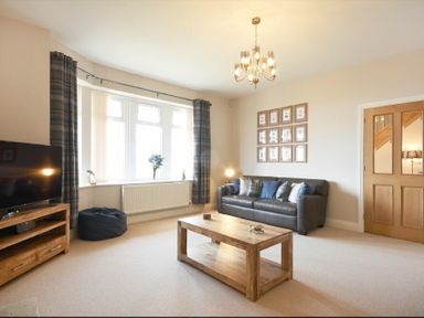 A living room with a leather sofa and wooden coffee table near a window with curtains and a television on a wooden stand at Bradacar in Seahouses