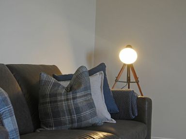 A sofa with cushions and a blanket next to a tripod floor lamp at Bradacar in Seahouses