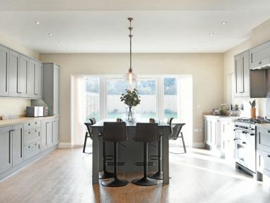 A kitchen with grey cabinets a central island with stools and large windows at Bradacar in Seahouses